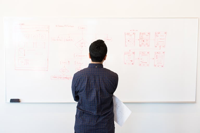 Man analyzing design flowchart on whiteboard in a professional office setting.